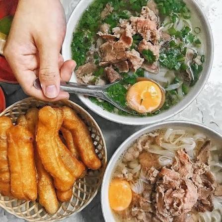 Hai tô phở bắc bò tái với bánh phở, thịt bò, rau xanh và nửa quả trứng, dùng kèm rổ quẩy chiên. – Không khí Hà Nội làm bát phở trở nên trọn vẹn hơn